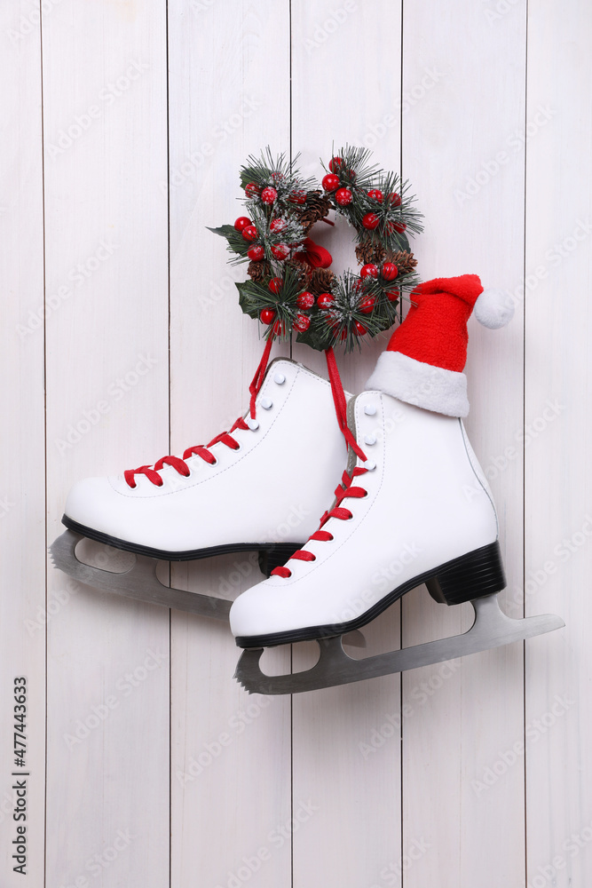 Obraz premium Pair of ice skates with Santa hat and Christmas wreath hanging on white wooden wall