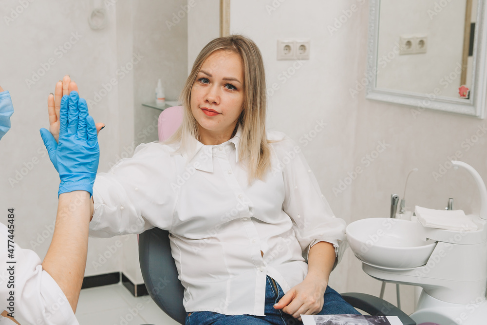 the blonde sits in a chair in the dentist's office and touches the doctor's hand to compromise that she will definitely recover after the treatment process. - obrazy, fototapety, plakaty 