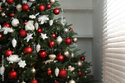Beautifully decorated Christmas tree near window indoors © New Africa
