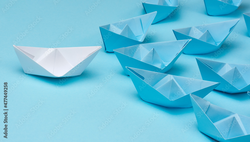 group of blue paper boats follow white against a light blue background. Strong leader concept, mass manipulation. Starting a business with a well-coordinated team, start-up group of blue paper boats follow white against a light blue background. Strong leader concept, mass manipulation. Starting a business with a well-coordinated team, start-up