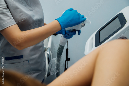 A master or cosmetologist in blue gloves wipes the workplace with an antiseptic, preparing for the epilation procedure.