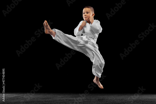 Dynamic portrait of little boy, young karate jumping isolated over white background. Concept of sport, education, skills