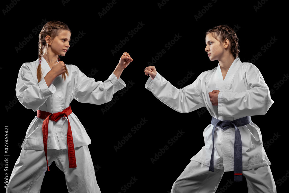Two young girls, teens, taekwondo athletes training together isolated over dark background. Concept of sport, education, skills Two young girls, teens, taekwondo athletes training together isolated over dark background. Concept of sport, education, skills