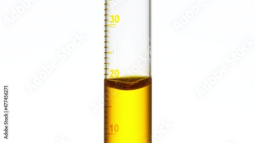 Drop of yellow fluid is falling down into graduated cylinder with yellow transparent fluid on white background | Abstract face care cosmetics formulation concept photo