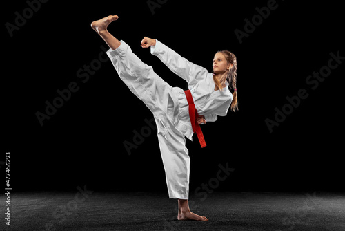 Flyer. Portrait of young girl, teen, taekwondo athlete practicing alone isolated over dark background. Concept of sport, education, skills © master1305