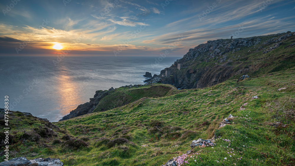 The dramatic Cornish coastline, near Lands End, with the ruins of the Botallack Tin mines, in the distance, framed against the setting sun.