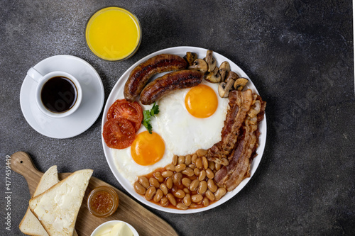 Full english breakfast with fried eggs, sausage, mushrooms, beans, toast and coffee on a dark background, top view