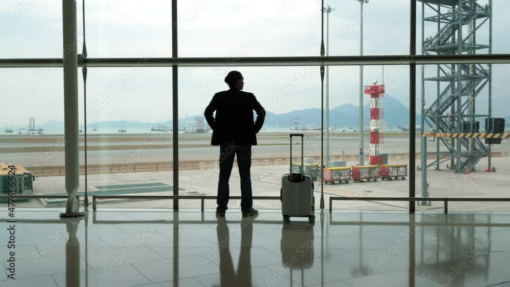 Man make step to window and stand against, look out to apron and empty taxiways. Passenger take breath after long international flight, rest at arrival terminal passage Man make step to window and stand against, look out to apron and empty taxiways. Passenger take breath after long international flight, rest at arrival terminal passage