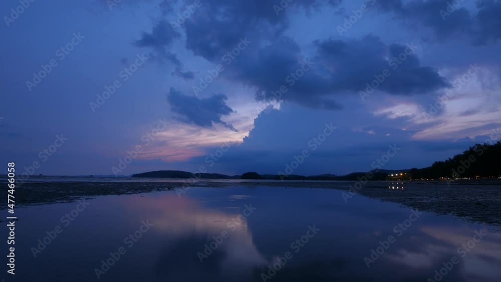 Blue clouds fly away on sky, big cumulonimbus cloud seen at horizon, reflection in puddle. Low tide after sunset, sea coast at Ao Nang beach, time lapse shot from dusk to night Blue clouds fly away on sky, big cumulonimbus cloud seen at horizon, reflection in puddle. Low tide after sunset, sea coast at Ao Nang beach, time lapse shot from dusk to night