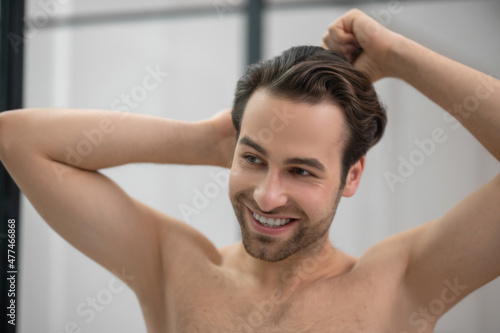 Young handsome man brushing his hair and looking contented