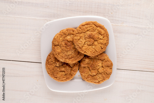 Several sweet homemade cookies with a white ceramic saucer  on a wooden table, close-up, top view.