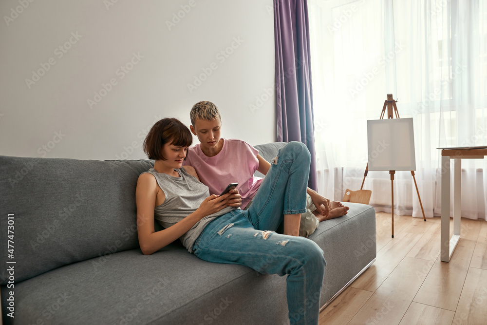 Lesbian girls watch on smartphone on sofa at home