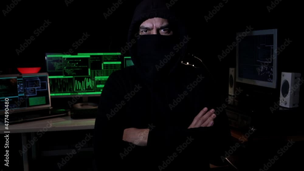 Cyber hacker with hood and covered face looks at the camera with serious look. Cyber terrorism concept. Cyber hacker with hood and covered face looks at the camera with serious look. Cyber terrorism concept.