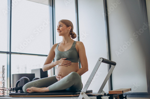 Pregnant woman exercising with the help of reformer on pilates class photo