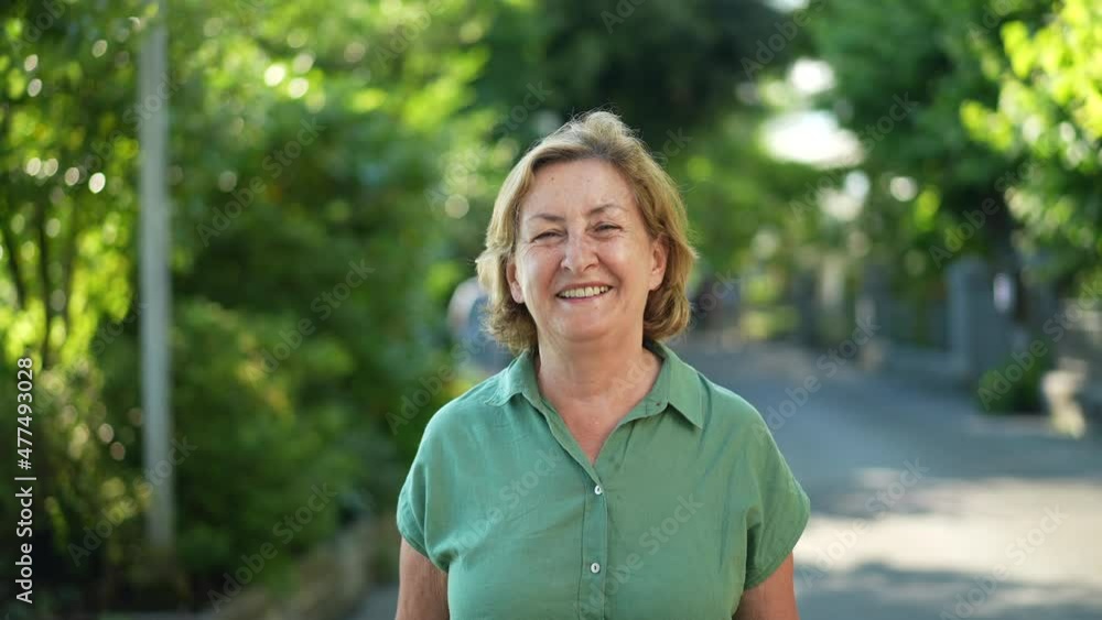 Happy senior woman walking forward smiling in city nature Happy senior woman walking forward smiling in city nature