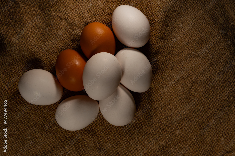 Chicken eggs are white and brown, stacked on a textured substrate. Farm chicken eggs, on burlap, matting. Chicken eggs are white and brown, stacked on a textured substrate. Farm chicken eggs, on burlap, matting.