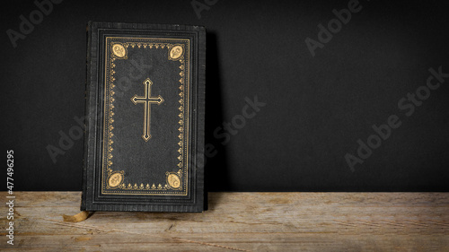 Church faith Christian background - Old holy bible with golden cross on old rustic vintage wooden table and black wall