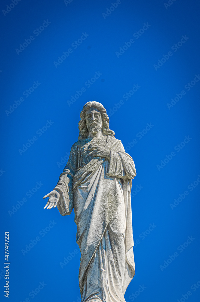 Cemetery statue of a saint against a blue sky.
