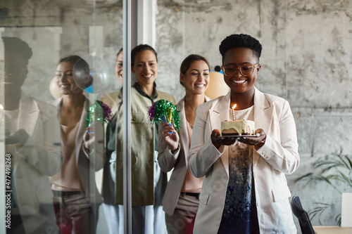 Happy black businesswoman carries cake while celebrating Birthday with her colleagues in the office. photo