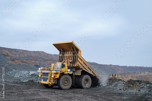 A large yellow dump truck unloads minerals. The process of mining and transportation of minerals. Ore mining by open-pit method.