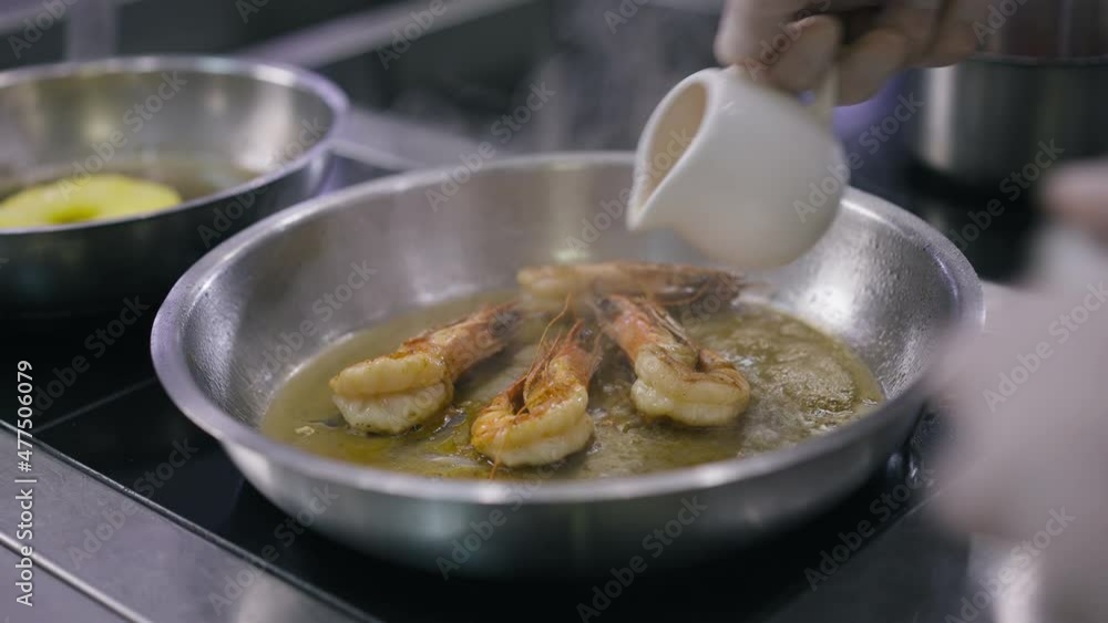 Close-up pouring igniting oil in cooking pan with grilled shrimps in slow motion. Unrecognizable professional Caucasian male chef cook preparing tasty seafood in restaurant kitchen indoors Close-up pouring igniting oil in cooking pan with grilled shrimps in slow motion. Unrecognizable professional Caucasian male chef cook preparing tasty seafood in restaurant kitchen indoors