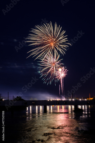 Fireworks over river with bridge and reflections.