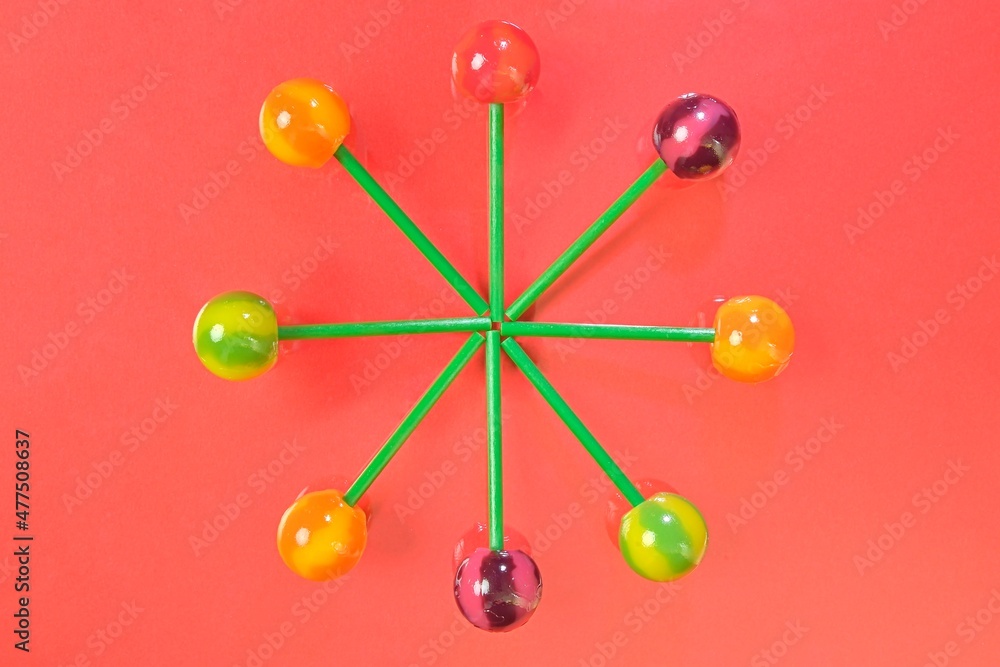 Tasty lollipops on coral pastel color background. Set of realistic colorful lollipops on green plastic sticks. Summer and pop art concept. Top view. Real reflection