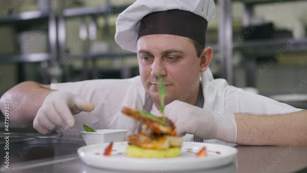 Portrait of satisfied positive chef decorating cooked seafood standing up. Happy confident professional Caucasian man in uniform serving delicious tasty dinner in restaurant kitchen Portrait of satisfied positive chef decorating cooked seafood standing up. Happy confident professional Caucasian man in uniform serving delicious tasty dinner in restaurant kitchen
