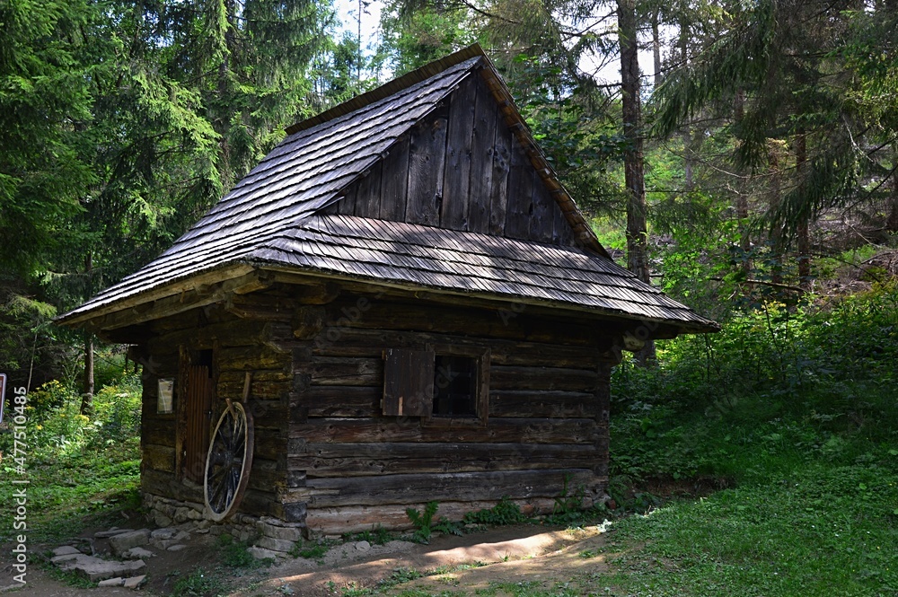 Small wooden blacksmith hut in woods of Orava region of northern Slovakia, some wheel visible in front of the doors. Location Vychylovka outdoor museum, Orava, northern Slovakia. Small wooden blacksmith hut in woods of Orava region of northern Slovakia, some wheel visible in front of the doors. Location Vychylovka outdoor museum, Orava, northern Slovakia.