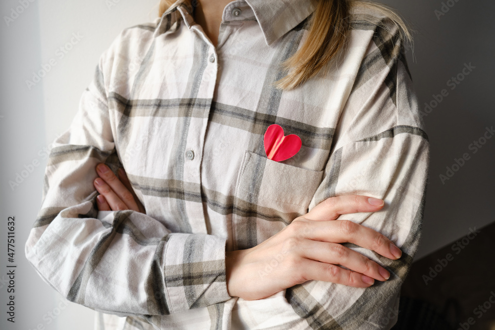 The girl holds a paper red heart in the chest area. The concept of love, Valentine's day, romance. Heart in a shirt pocket. I'm looking for a partner!