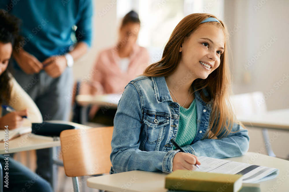 © Drazen - Smiling teenage girl takes notes during a class in high school.