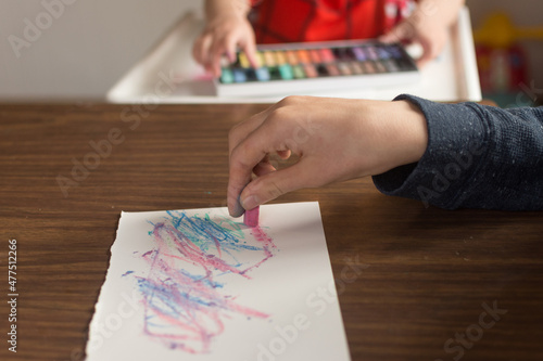 Brother and sister make art side by side; toddler and young boy draw with chalk pastels on paper