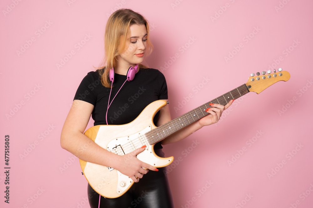 Young woman playing the electric guitar standing over pink background. Young woman playing the electric guitar standing over pink background.