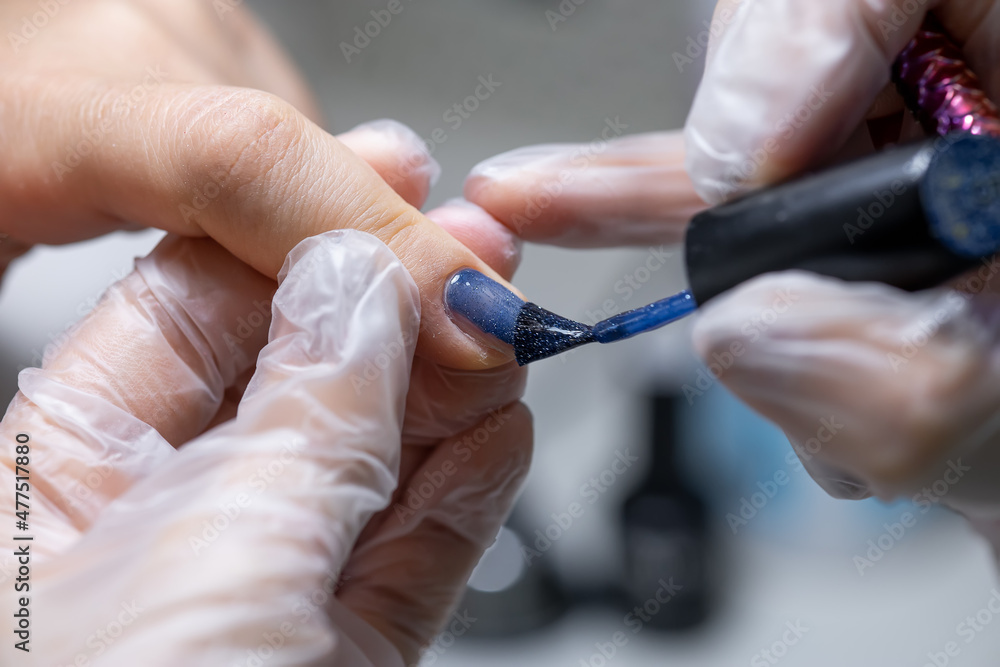the nail service master makes a manicure by distributing blue gel polish with a nail brush on the nail surface the nail service master makes a manicure by distributing blue gel polish with a nail brush on the nail surface