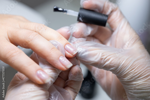 the nail service master does a manicure holds his finger and applies a transparent gel polish to protect the nail