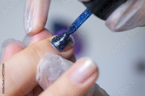 the nail service master does a manicure and applies the first layer of blue gel polish