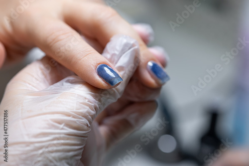 the master of the nail service makes a manicure close-up nails on which a blue gel polish is applied