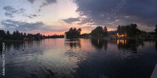 Beautiful blue and pink sunset over the lake with trees, ducks, grass, park and water fountain.