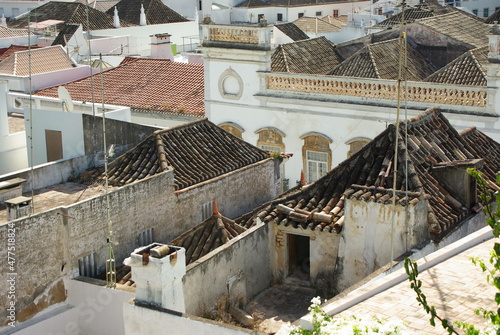 View from above to a deteriorated tiled building roof and a street in Tavira,