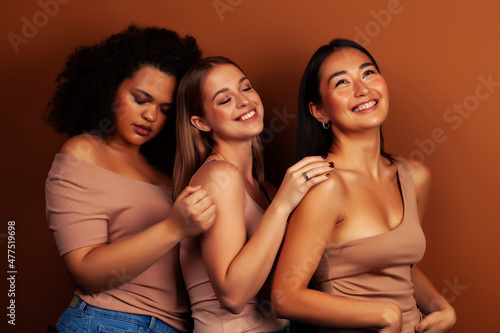 young pretty asian, caucasian, african woman posing cheerful together on brown background, lifestyle diverse nationality people concept