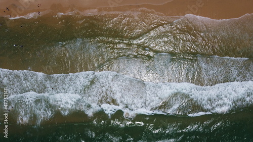 Ocean waves and sandy beach on sunny day. Aerial view