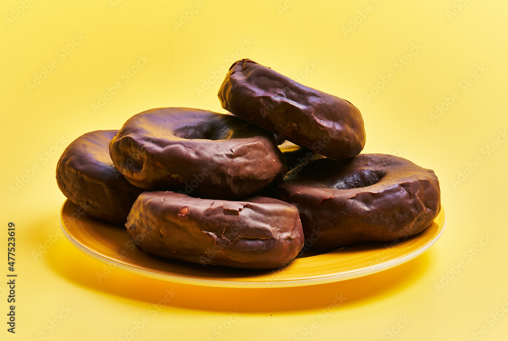 Plate of chocolate doughnuts over yellow background Plate of chocolate doughnuts over yellow background