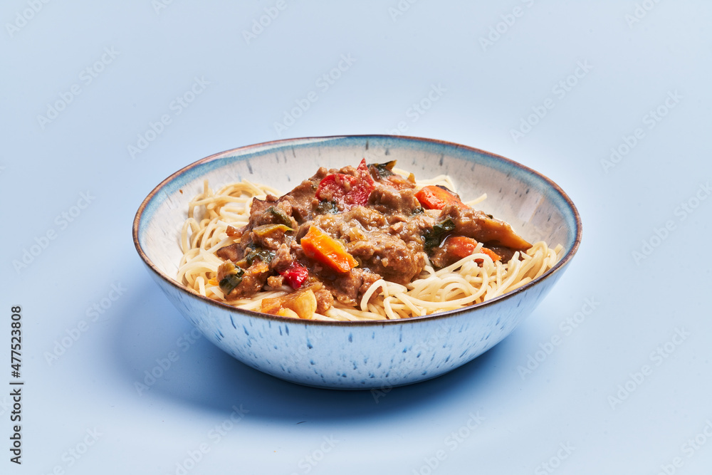Plate of delicious spaghettis with meat and vegetables over blue background Plate of delicious spaghettis with meat and vegetables over blue background