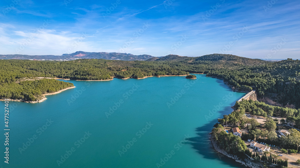 expanse of water island with green trees sun over water reflection islet blue water vegetation shore aerial view drone photography horizon with mountains sunny blue sky