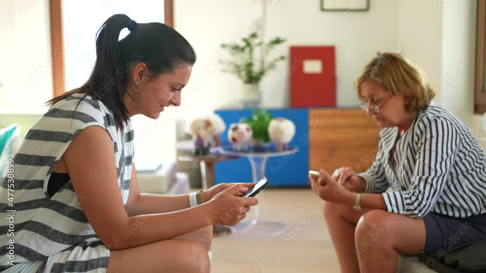 Two women looking at cellphone devices. Two people staring at smartphone separately Two women looking at cellphone devices. Two people staring at smartphone separately