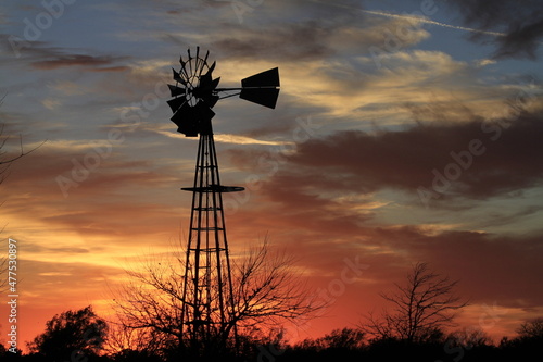 Kansas Sunset with a colorful sky with clouds and a farm Windmill silhouette that's bright and colorful. That's north of Hutchinson Kansas USA.