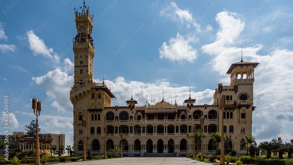 The ancient Montazah Royal Palace with arched openings and columns in the park of Alexandria. Tall towers against the blue sky. The lights stand along the driveway. Egypt