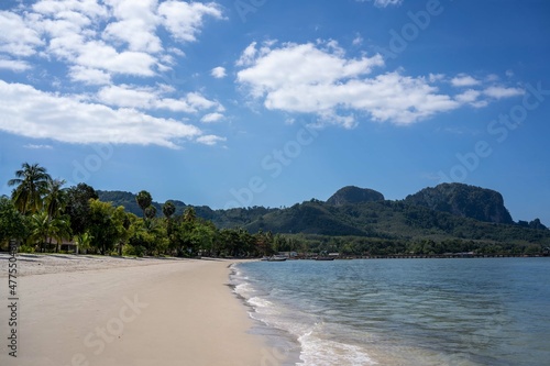 Beautiful beach of Thailand. White sand and the blue ocean with the trees and the mountain on the background.