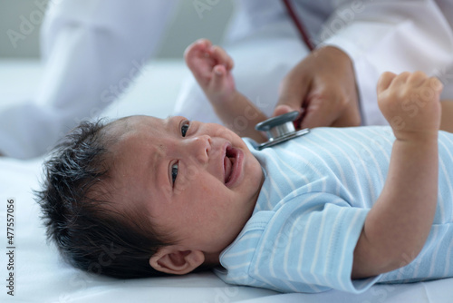 Pediatric doctor exams newborn baby girl at home, doctor listens to the heart with a stethoscope