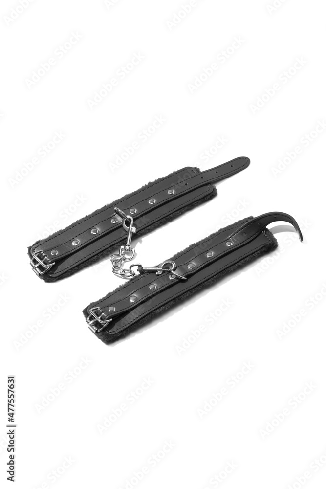Detailed shot of unbuckled black handcuffs with steel rivets, buckles and faux fur inside. The wristbands are connected by a steel chain and isolated on the white background. Detailed shot of unbuckled black handcuffs with steel rivets, buckles and faux fur inside. The wristbands are connected by a steel chain and isolated on the white background.